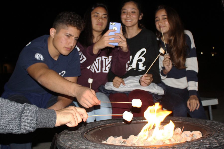 Sophomores gather around a fire pit roasting marshmallows for smores. Instead of sleeping over, sophomores spent an early night bonding with their class and their family.