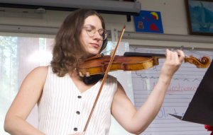 Karolina plays her violin, pulling her bow across the strings to create sounds.
